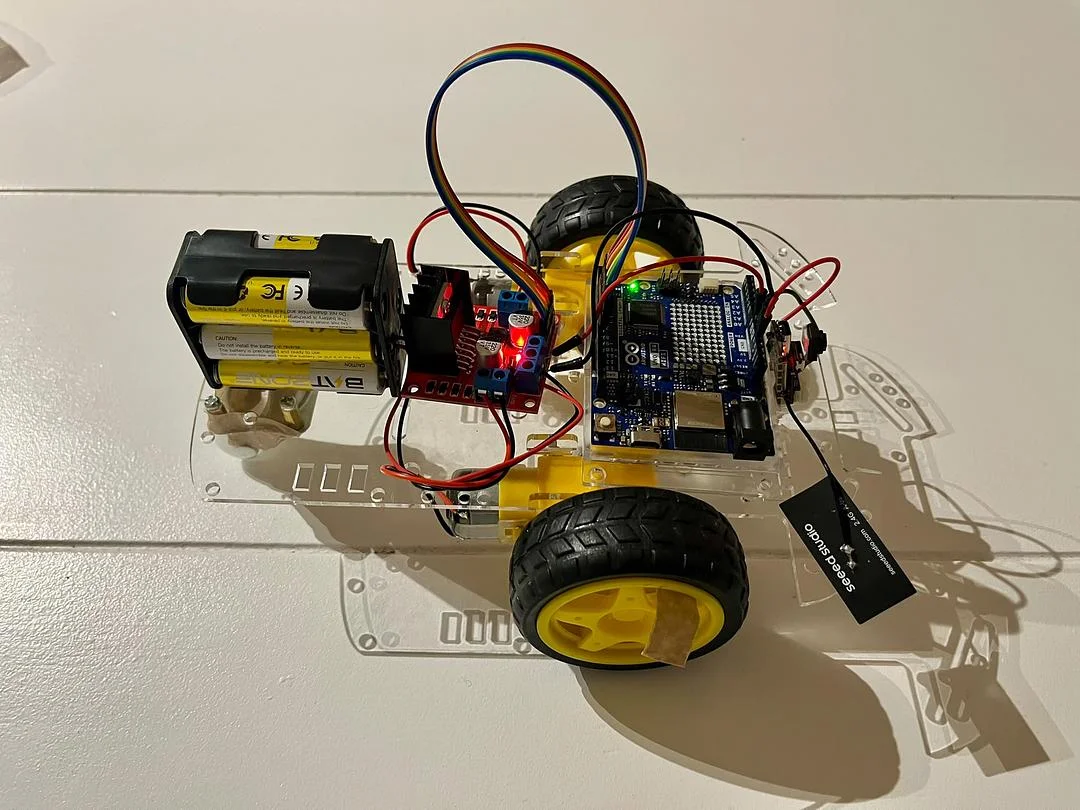 A small robot toy car with exposed electronics; a tiny camera is attached to its right side